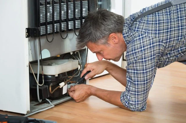 Refrigerator repair technician diagnosing an older refrigerator in Houston home
